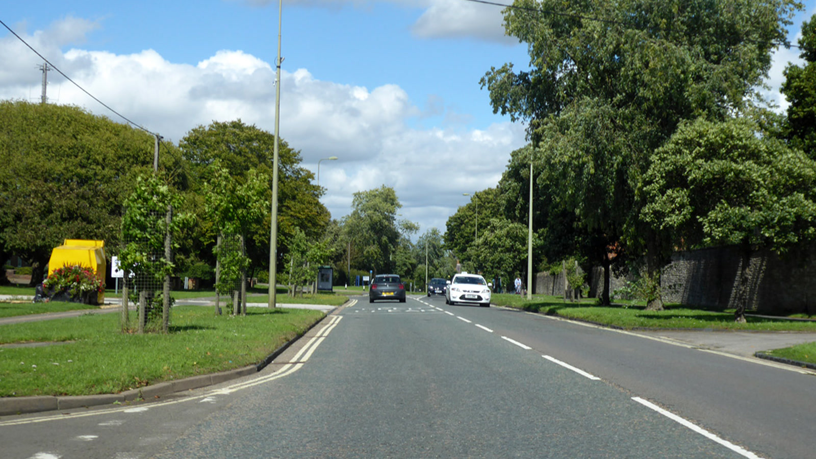 Tree-lined roadway along Queens Avenue in Bicester with streetlights and passing cars, photographed in August 2020.